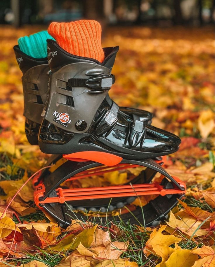 a pair of skis that are sitting on the ground with leaves around them and one has an orange sock attached to it