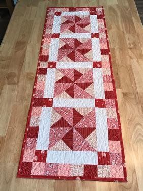 a red and white quilted table runner sitting on top of a wooden floor next to a window