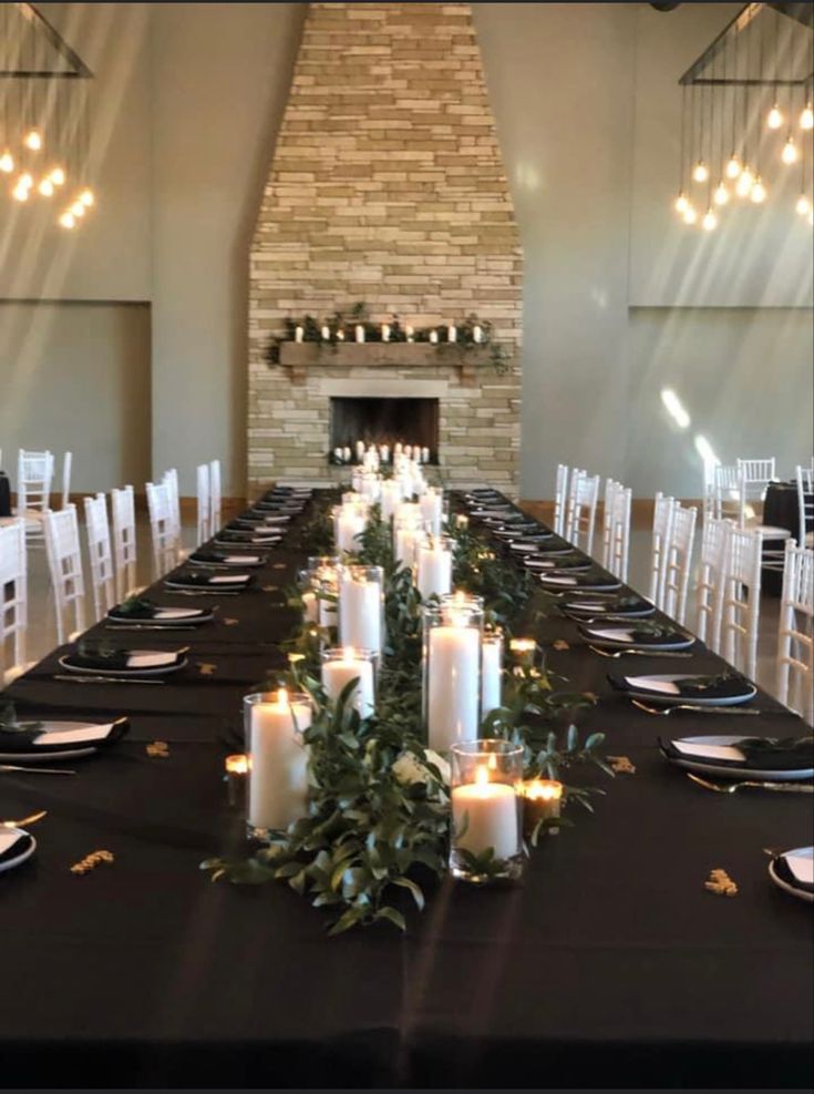 a long table is set with candles and place settings in front of the fireplace for an elegant dinner