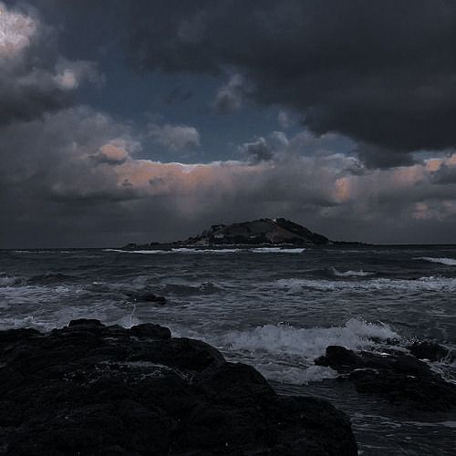 a black and white photo of the ocean with storm clouds in the sky over an island