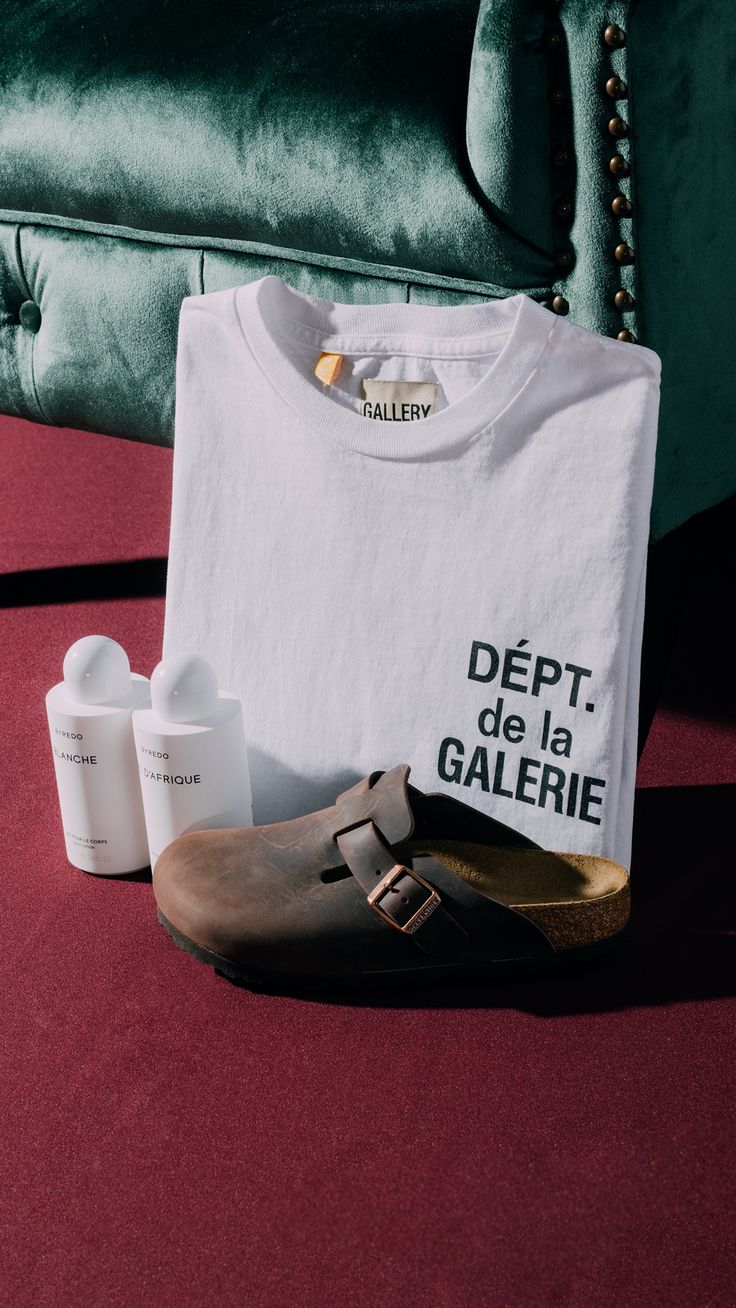 a t - shirt, shoes and lotion are on the floor in front of a couch