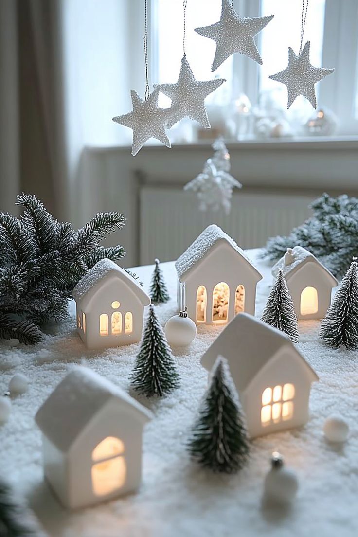 small white houses with lights in front of them on snow covered ground next to christmas trees