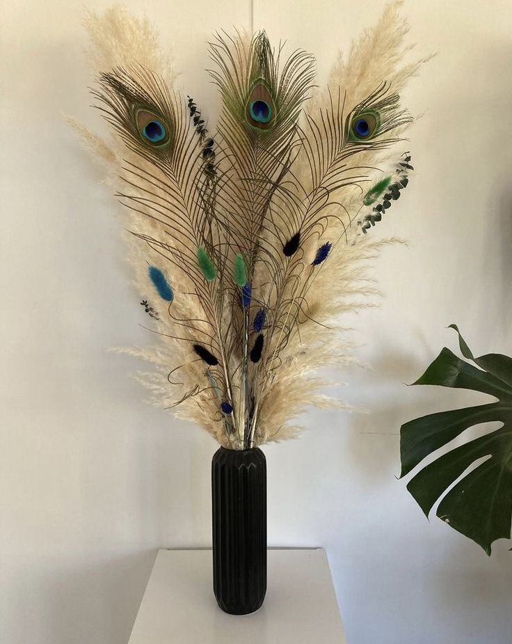 a vase with some feathers in it on a white table next to a potted plant