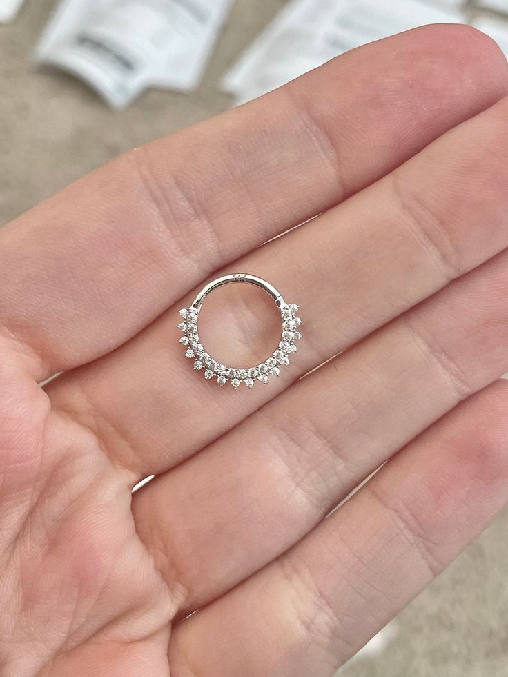 a person's hand holding an open ring with small white stones on the inside