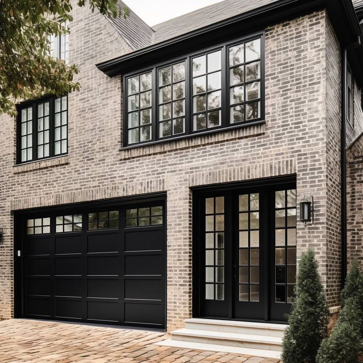 a large brick house with two black garage doors and windows on the side of it