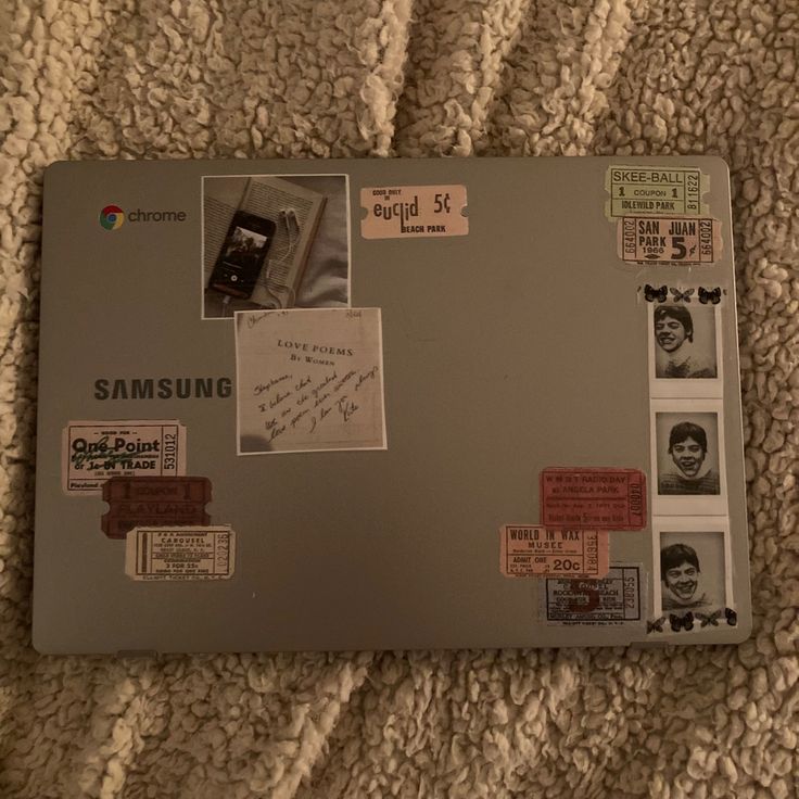 an open laptop computer sitting on top of a bed covered in lots of stickers