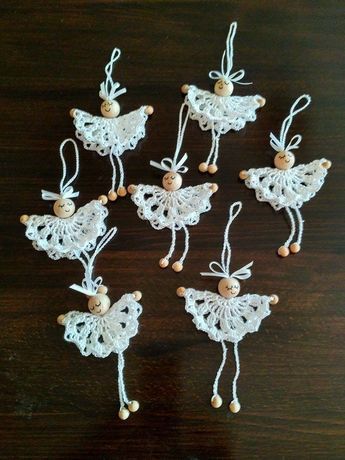 six crocheted angel ornaments with wooden buttons and string hangers on a table