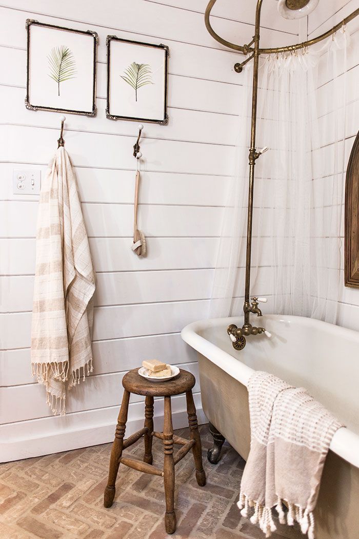 an old fashioned bathtub in a bathroom with white walls and wood flooring, two framed pictures on the wall