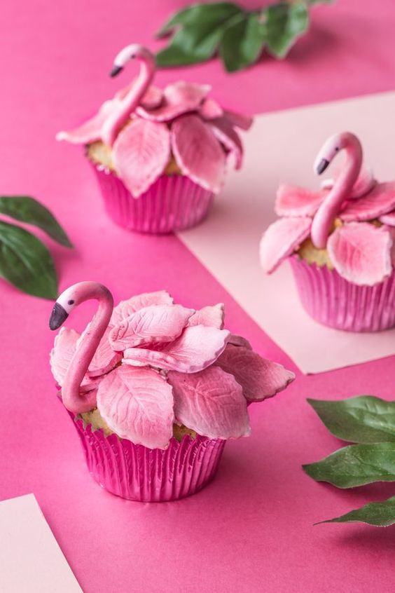 cupcakes decorated with pink flowers and flamingos are sitting on a pink surface