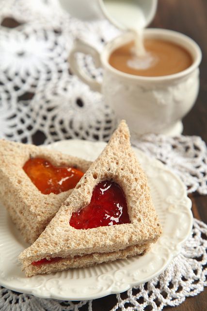 two sandwiches on a plate with jam in the middle and a cup of coffee behind them