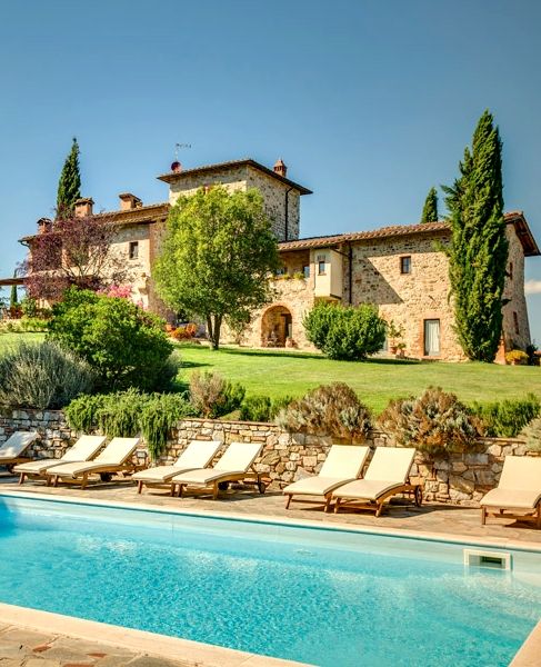 an outdoor swimming pool with chaise lounges in front of a large stone house