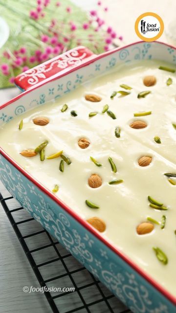 a blue and red dish with almonds on it sitting on a cooling rack next to flowers