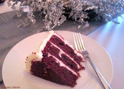 a slice of red velvet cake on a white plate with a fork and silver christmas tree in the background