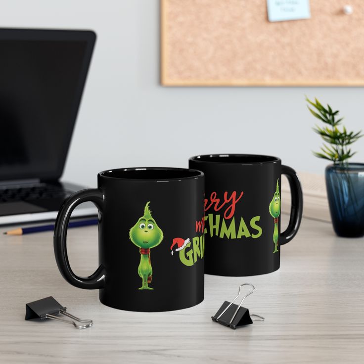 two black coffee mugs sitting on top of a desk next to a laptop computer