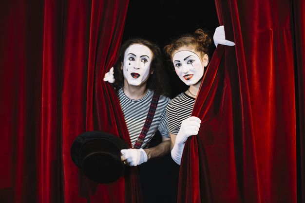 two people dressed as clowns peeking out from behind red curtains