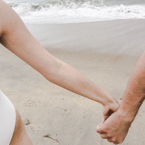 two people holding hands while walking on the beach