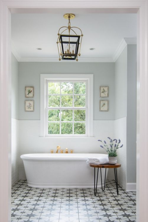 a white bath tub sitting under a window next to a table with flowers on it