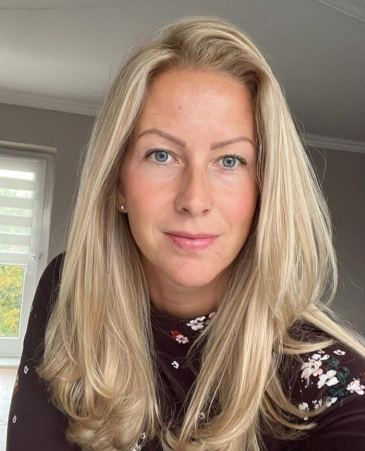 a woman with blonde hair and blue eyes posing for a photo in front of a window