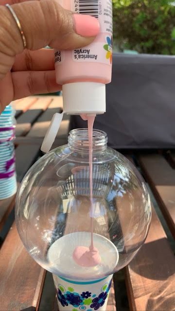 a hand is pouring liquid into a glass vase on top of a table with other items