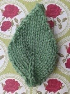 a close up of a knitted object on a tablecloth with roses in the background