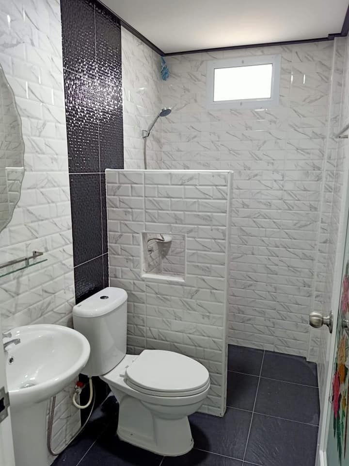 a white toilet sitting in a bathroom next to a sink and shower head mounted on a wall