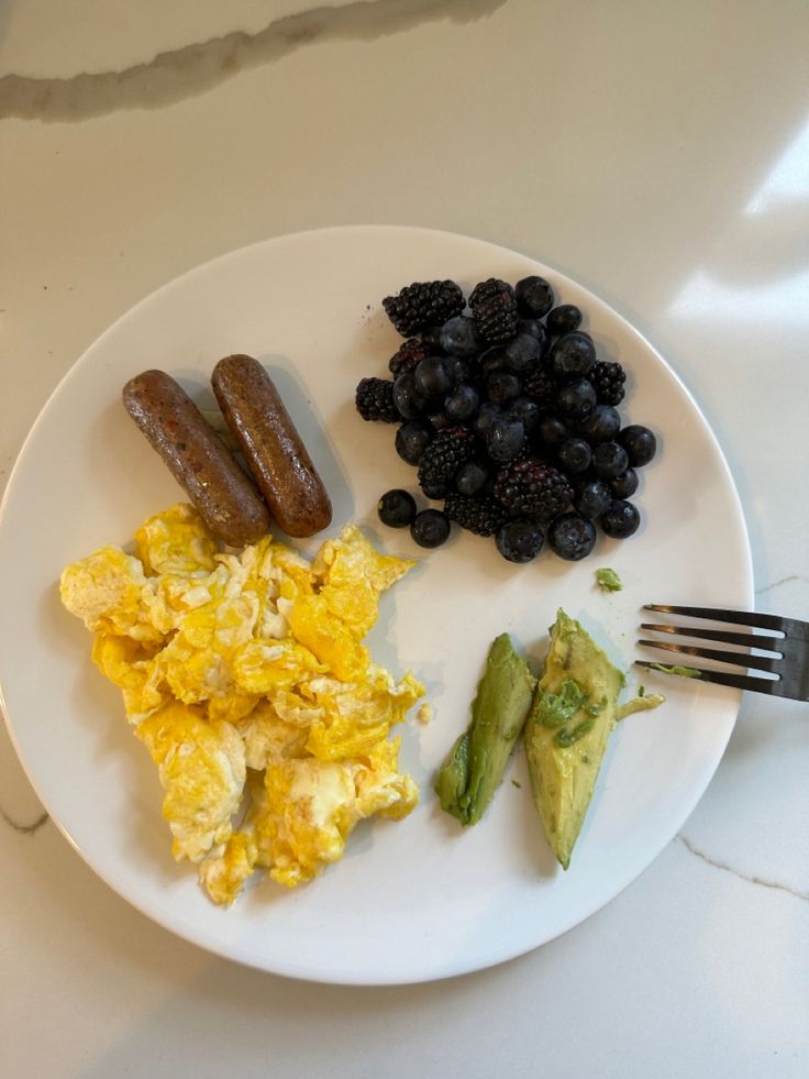 a white plate topped with eggs, berries and sausage next to an avocado