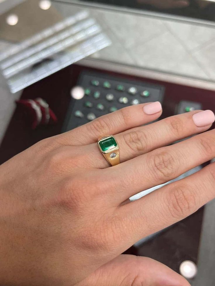 a woman's hand wearing a gold ring with a green stone on the middle