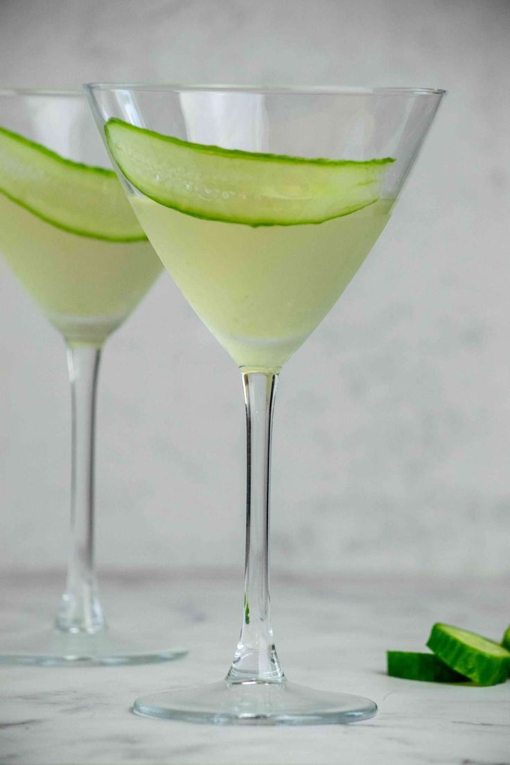 two martini glasses with cucumber slices on the rims, one filled with liquid