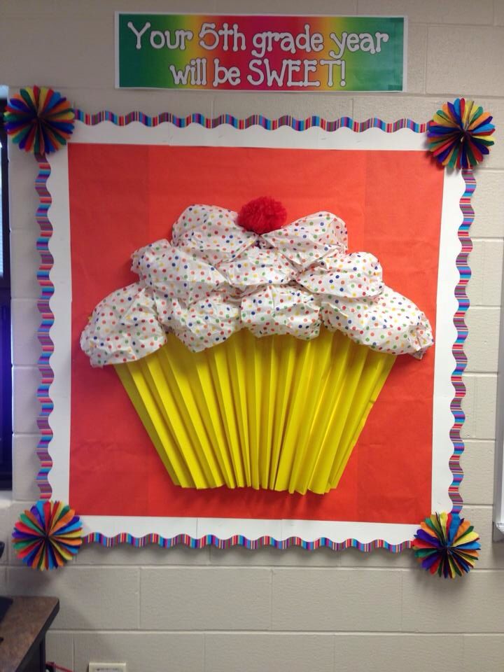 a cupcake with white frosting and sprinkles on it in front of a bulletin board