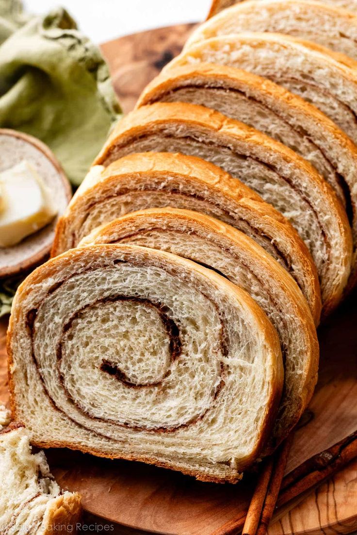 sliced cinnamon roll sitting on top of a wooden cutting board next to some bread sticks