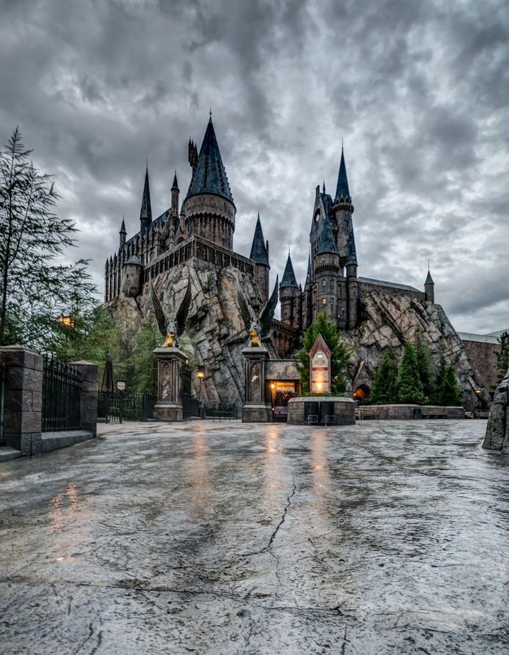 the hogwarts castle is lit up at night with its lights on and dark clouds in the sky