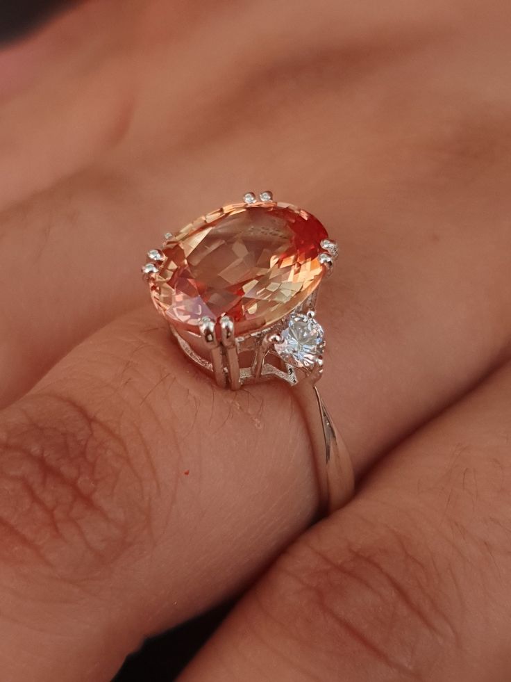 a woman's hand holding an orange and white ring with two diamonds on it