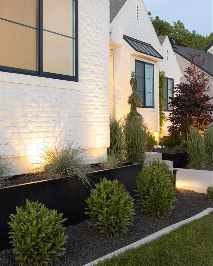 a white house with black planters and lights on the front porch, along with other plants