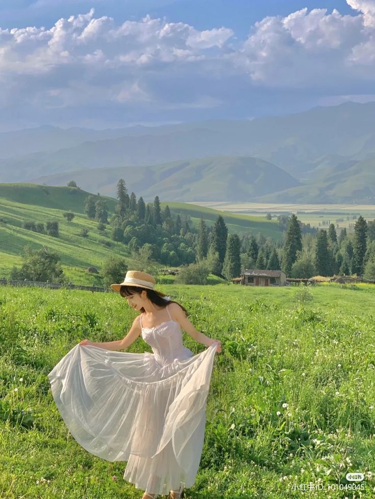 a woman in a white dress and hat is walking through the grass with her long flowing skirt