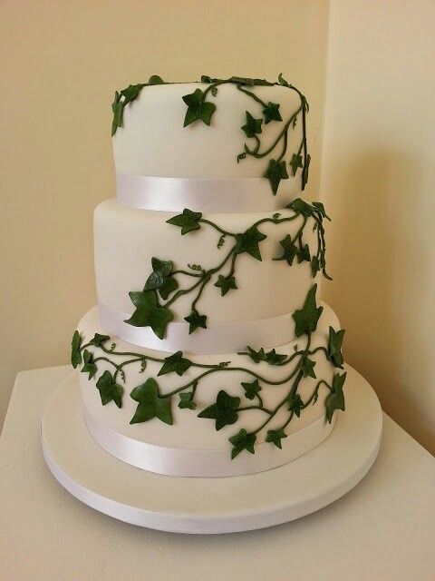 a three tiered white cake with green ivy on it's top and bottom