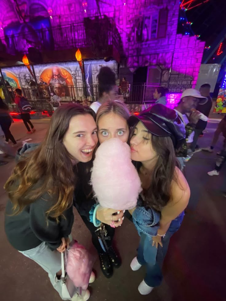 three girls are posing for the camera with a pink cotton candy in front of them