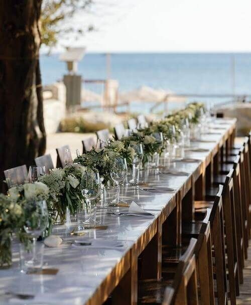 a long table is set up with place settings for an outdoor dinner by the beach