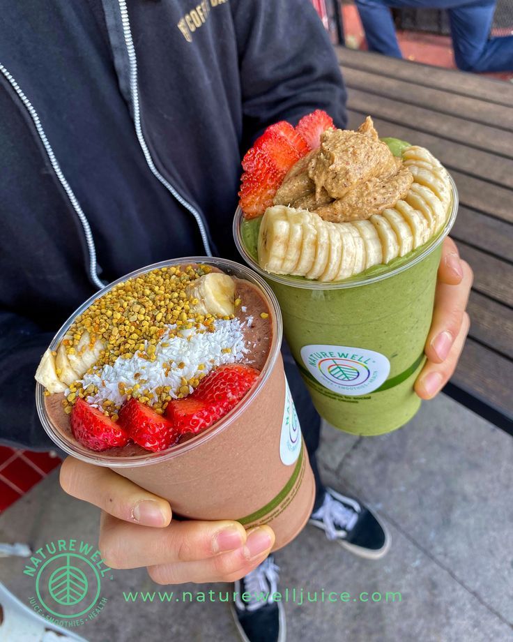 two people holding up cups with different types of food in them and one has a banana split on top