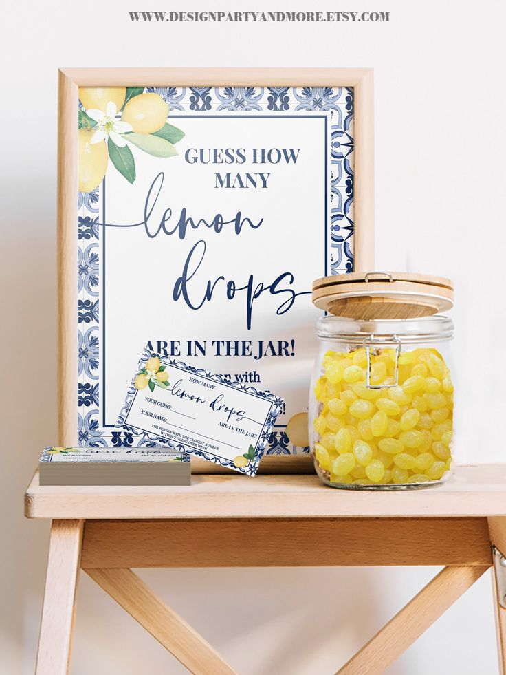 a wooden table topped with a jar filled with yellow candies next to a sign that says guess how many lemon drops are in the jar