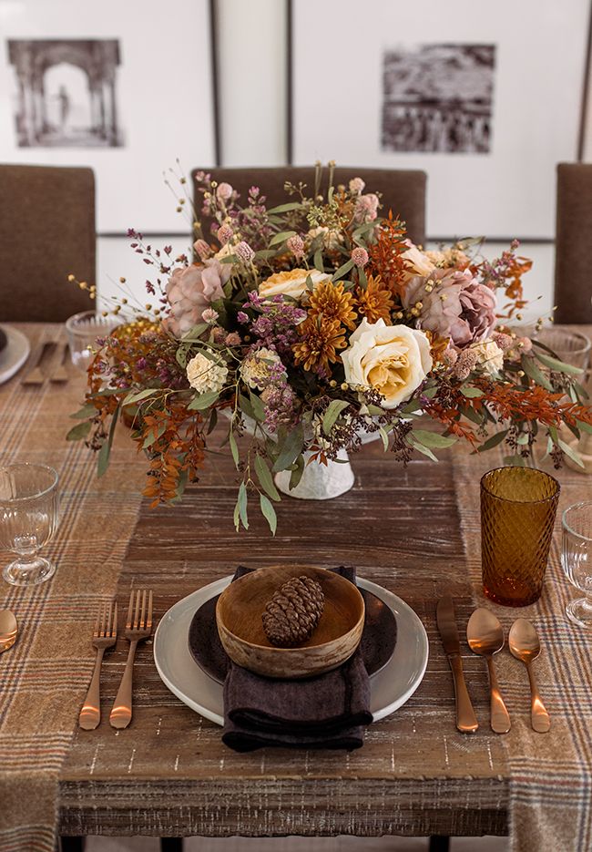 an arrangement of flowers in a vase on top of a table with plates and utensils