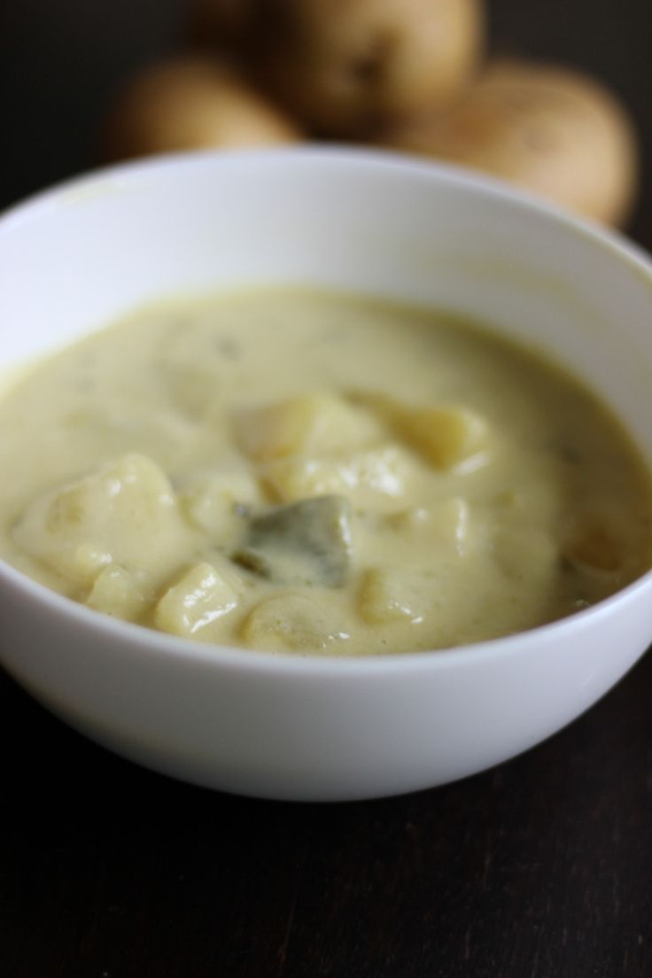 a white bowl filled with soup sitting on top of a table next to some potatoes