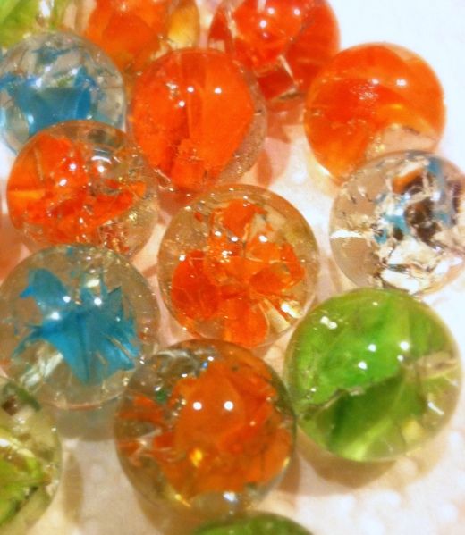 many different colored glass beads on a white tablecloth with green and orange flowers in the center