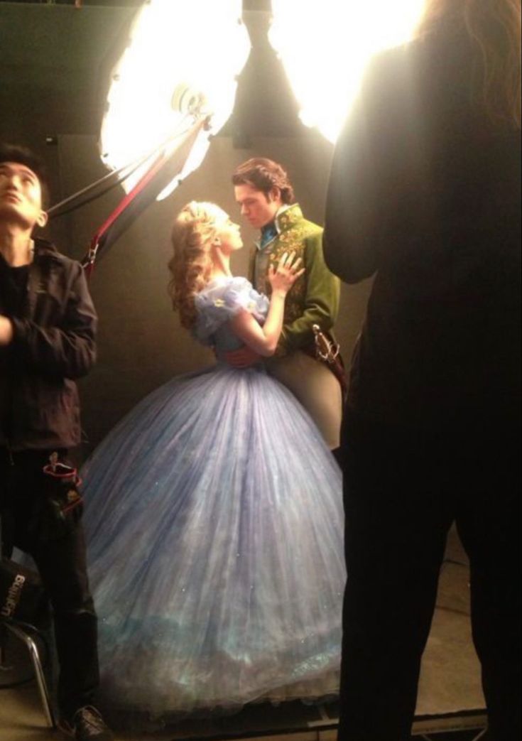 a woman in a ball gown is surrounded by photographers and lights as the man looks on