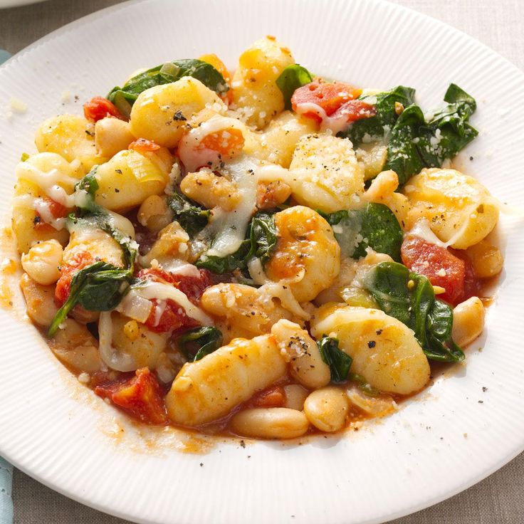 a white plate topped with pasta and spinach covered in sauce on top of a table