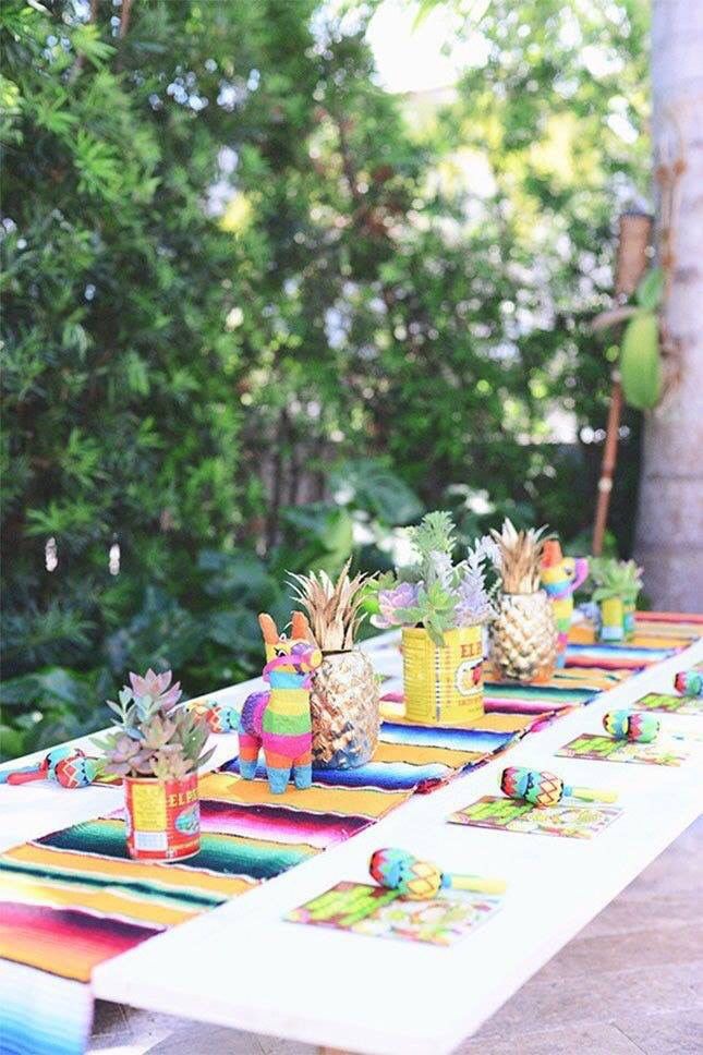 a long table with pineapples and colorful napkins on it in front of some trees