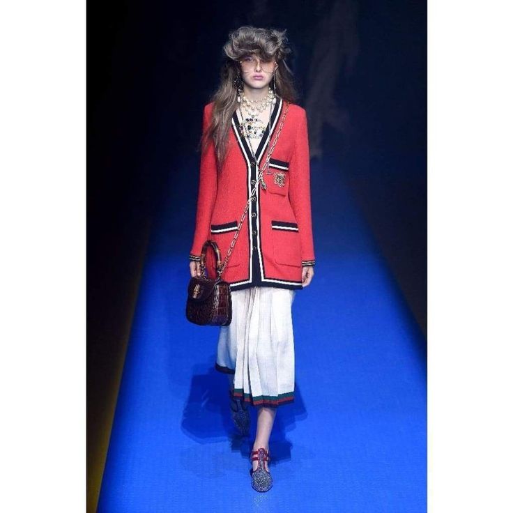 a woman is walking down the runway in a red coat