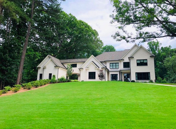 a large white house sitting in the middle of a lush green field with lots of trees