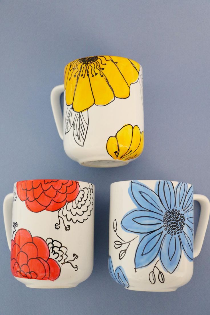 three coffee mugs with painted flowers on them are sitting in front of a blue background