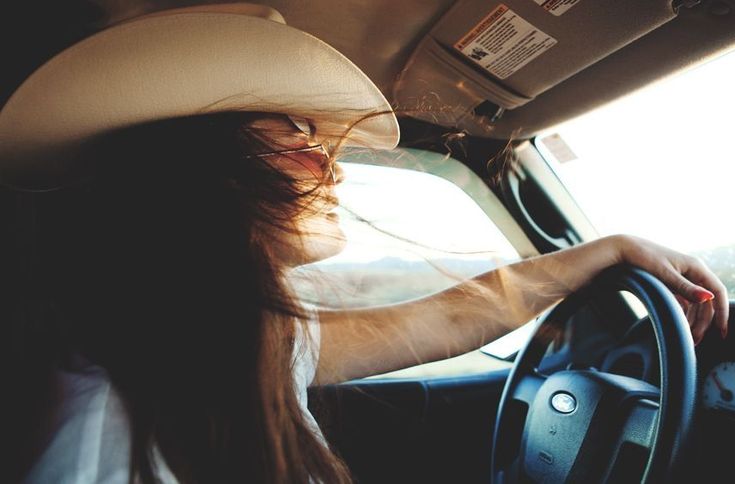 a woman wearing a cowboy hat driving a car with her hands on the steering wheel