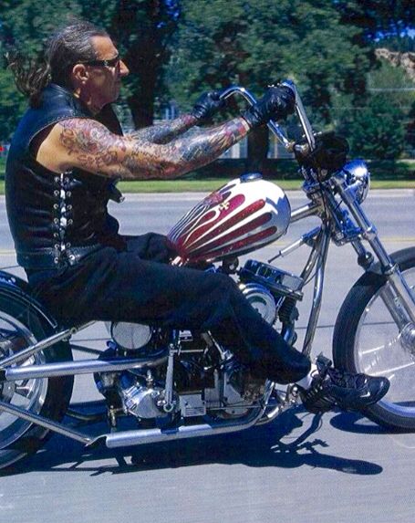 a man riding on the back of a motorcycle down a street with trees in the background